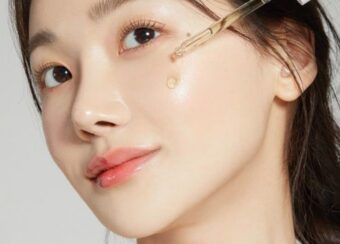 Woman applying facial serum with a dropper on her cheek, showcasing glowing and hydrated skin.